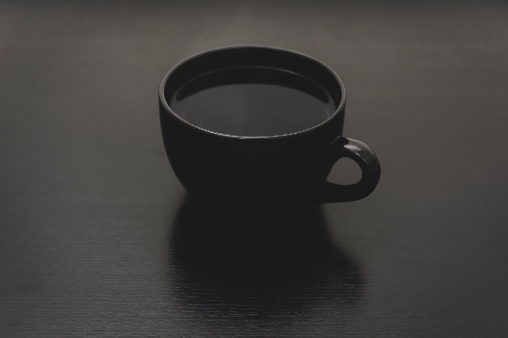 A cup of black coffee in a black mug on a black table