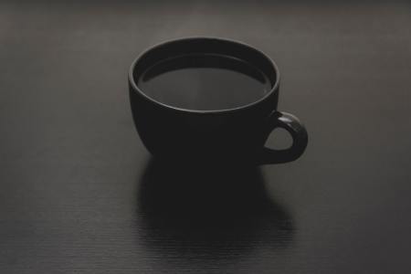 A cup of black coffee in a black mug on a black table