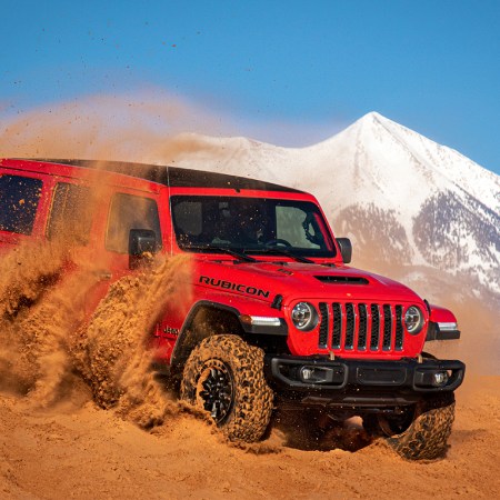 A red Jeep Wrangler Rubicon 392, the first-ever Wrangler with a V8 engine, churning up sand dunes in front of a snow-capped mountain