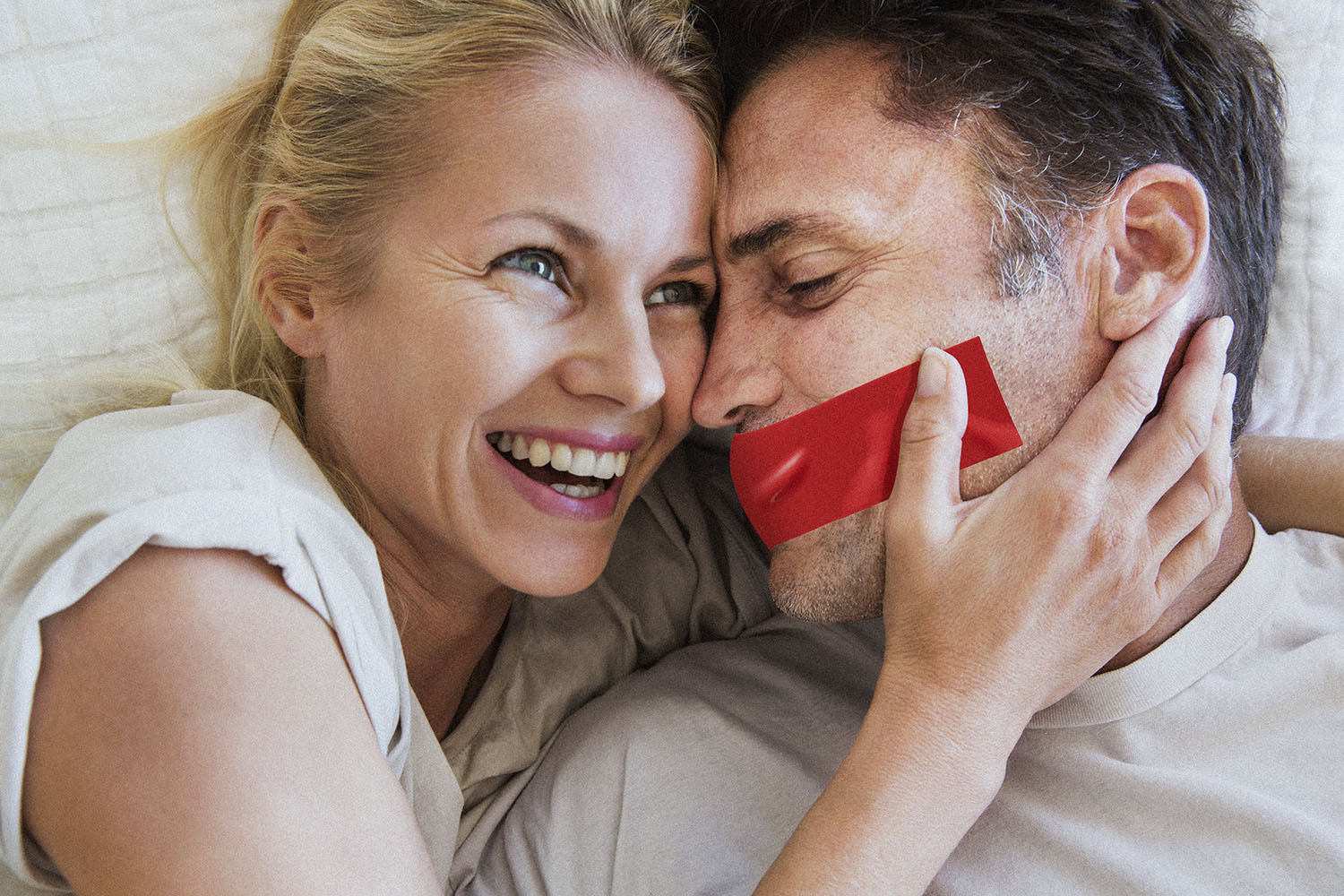 Couple in romantic embrace, woman laughing, man has tape over his mouth