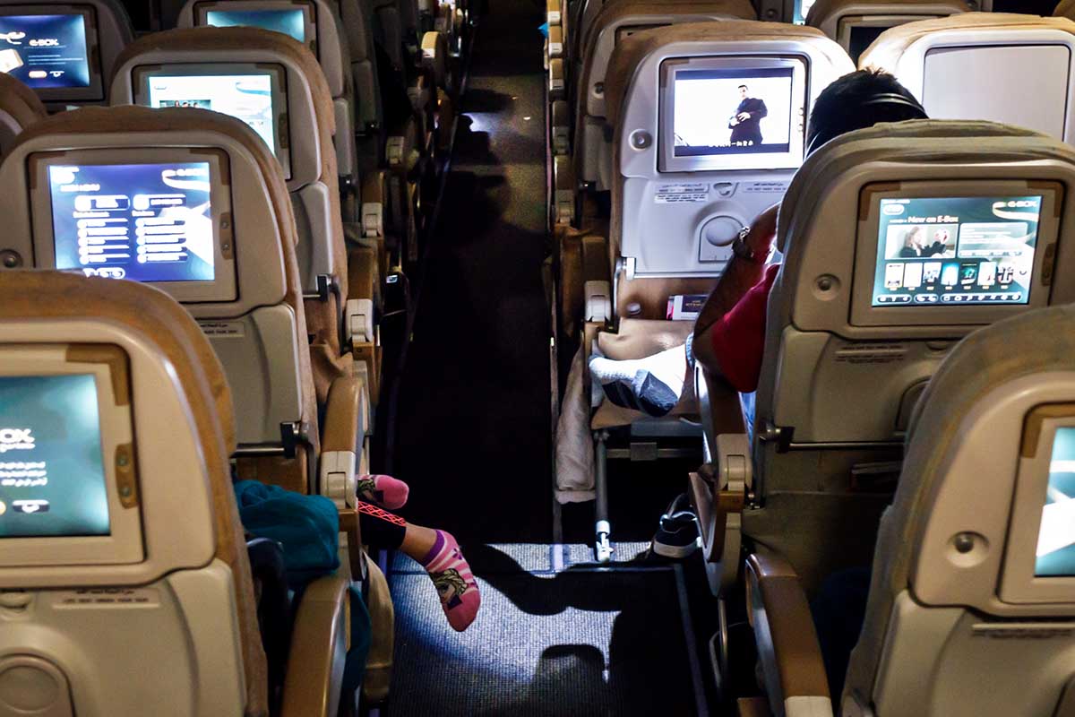United Arab Emirates, Abu Dhabi International Airport, onboard cabin economy class Etihad Airways flight girl sleeping feet dangling.