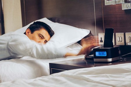 Businessman sleeping on bed and his hand reaching to turn off alarm clock with speedy action at 6:30 AM, Wake up early morning concept. Hotels with alarm clocks may soon become a thing of the past.