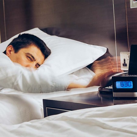 Businessman sleeping on bed and his hand reaching to turn off alarm clock with speedy action at 6:30 AM, Wake up early morning concept. Hotels with alarm clocks may soon become a thing of the past.
