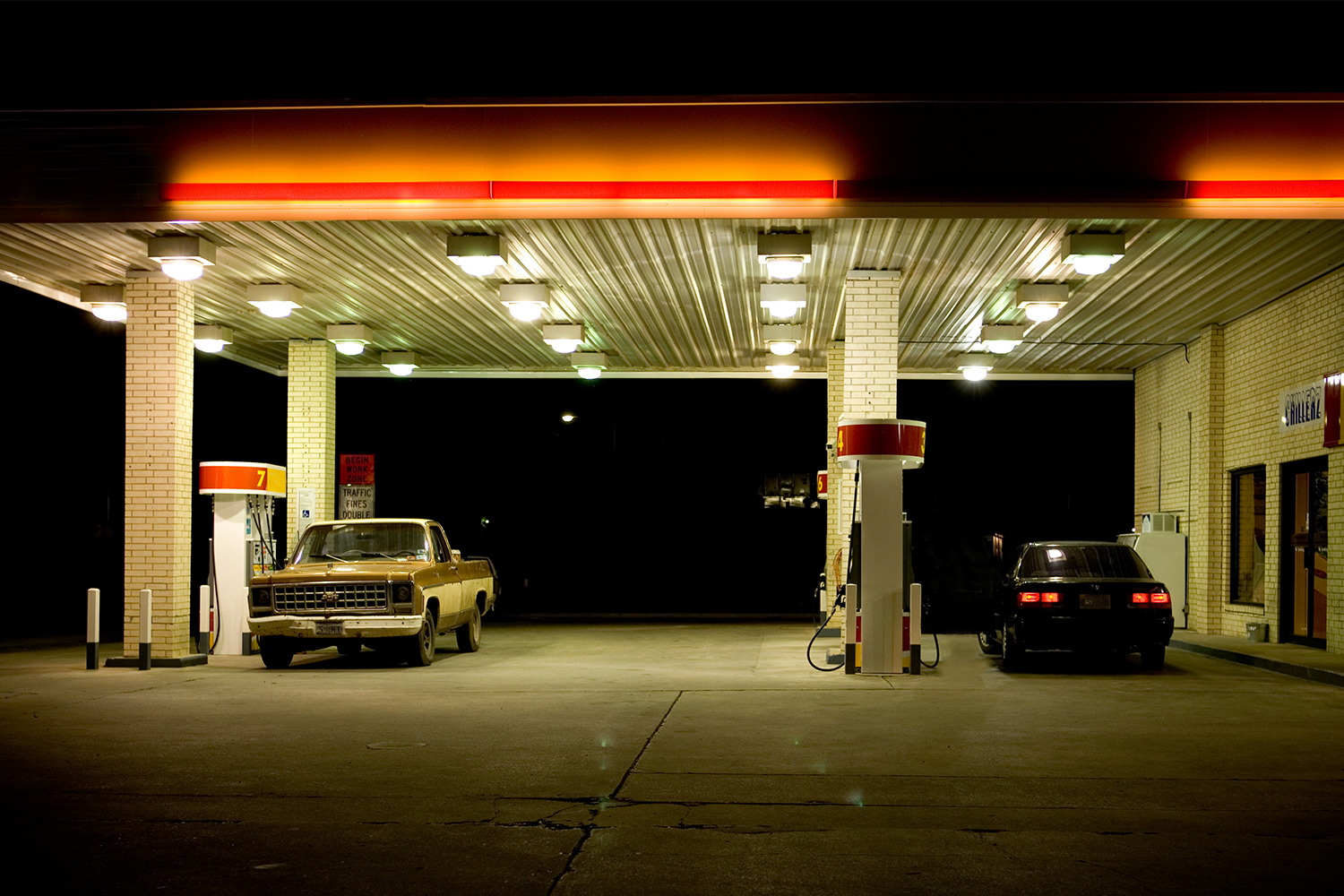 A pickup truck and black car at a gas station at night. Our love of gasoline is a problem when it comes to climate change.