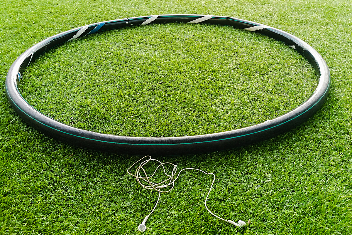 A weighted hula hoop, used for a trendy workout called hooping, sitting in the grass next to earbuds