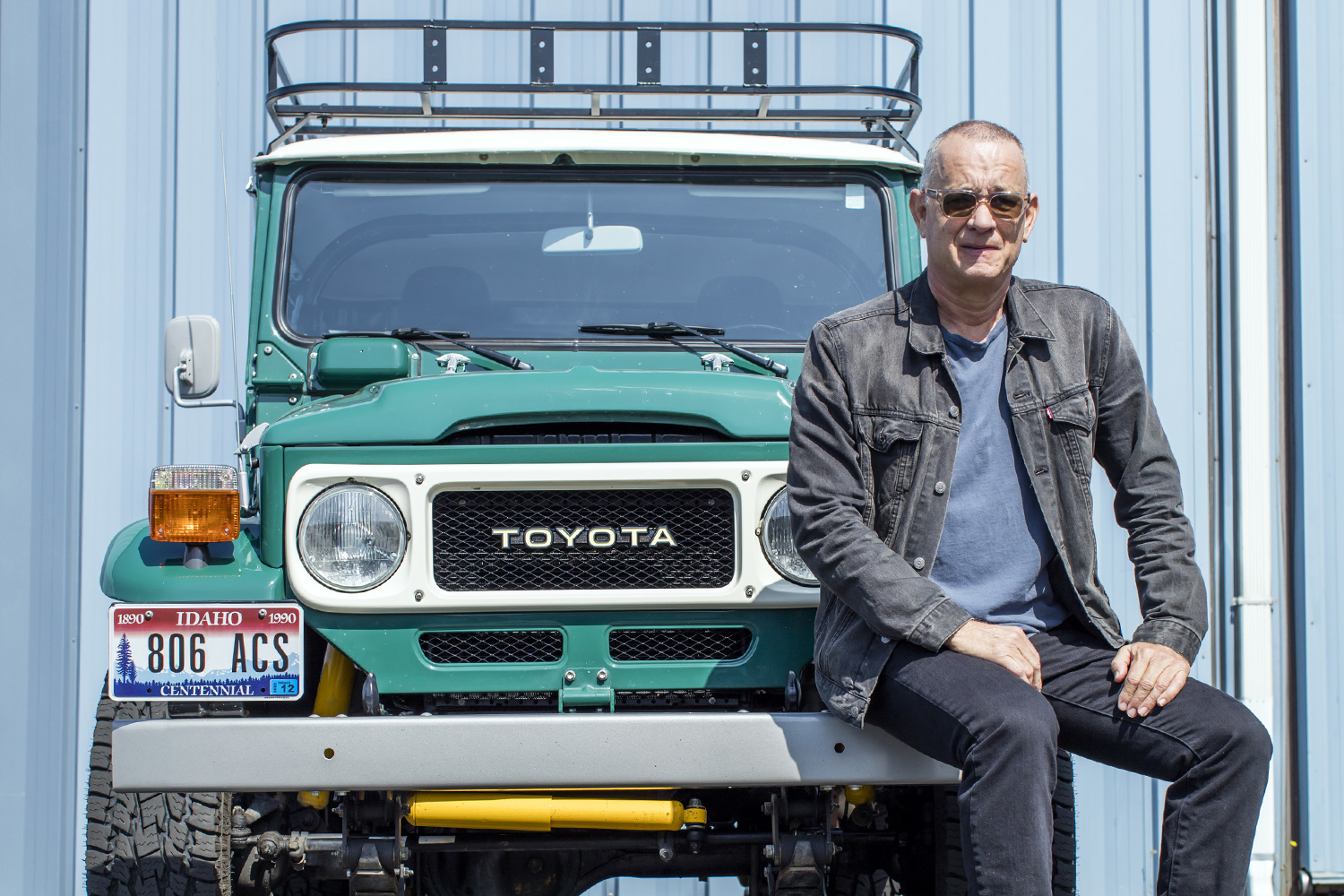 Actor Tom Hanks sitting on the bumper of his Toyota FJ40 Land Cruiser. The custom SUV, from TLC 4x4 and ICON 4x4, is headed to auction at Bonhams.