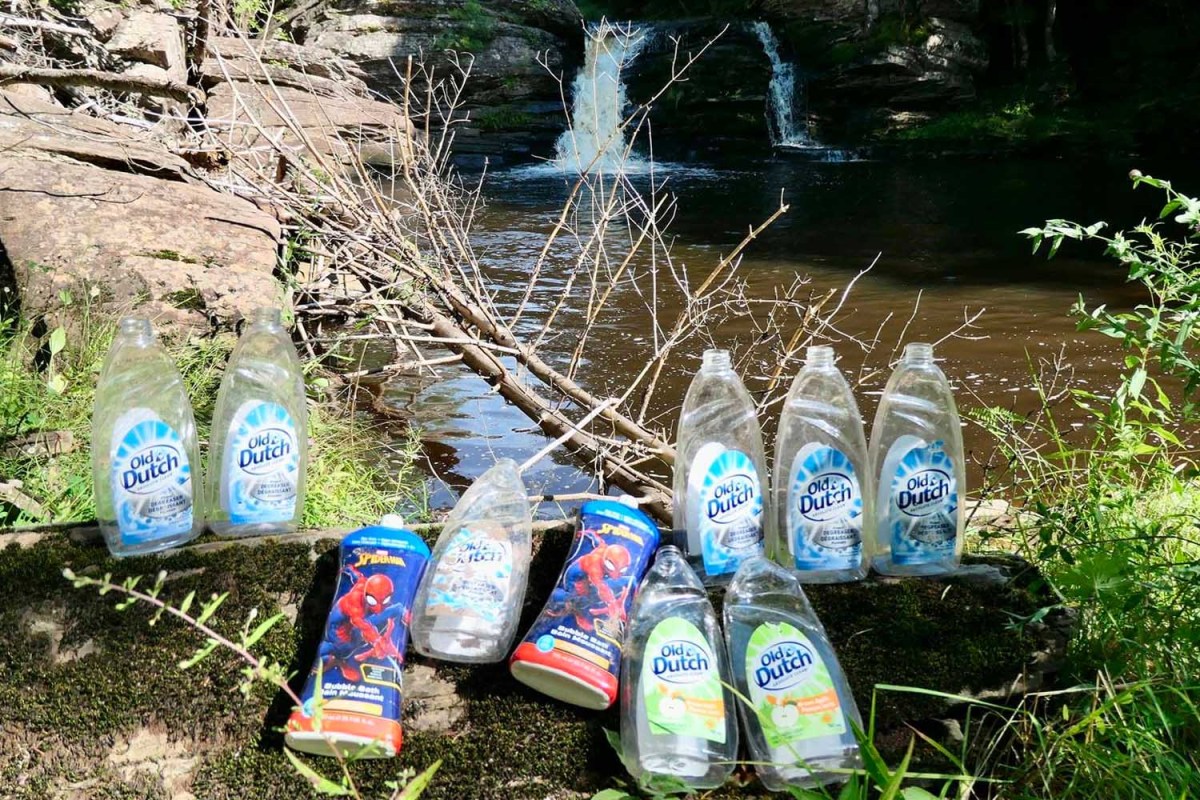 ten bottles of empty dish soap containers sit near a water fall in Nova Scotia