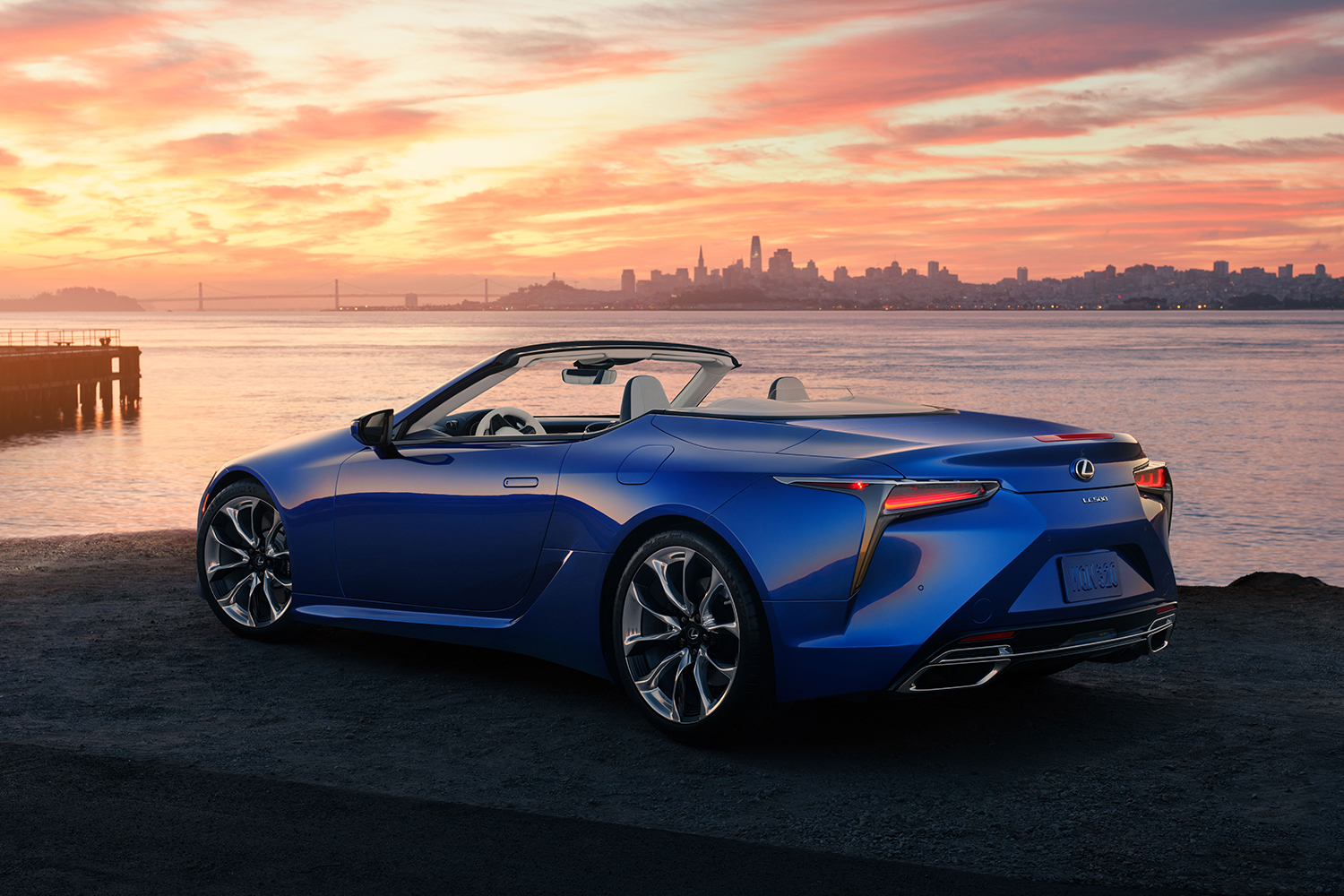 The rear end of a blue The Rear End of the 2021 Lexus LC 500 Convertible with a city and sunset in the background. We test drove the grand tourer and wholeheartedly recommend it.