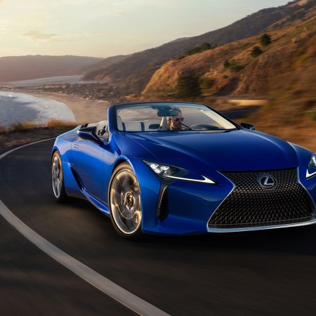 A man driving a blue 2021 Lexus LC 500 Convertible down a coastal road. The luxury grand tourer has become one of our favorites after test driving.