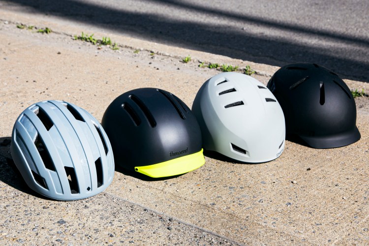 Four stylish, modern bicycle helmets — by Sweet Protection, Thousand, Smith and Bern, respectively — situated in a row on the sidewalk