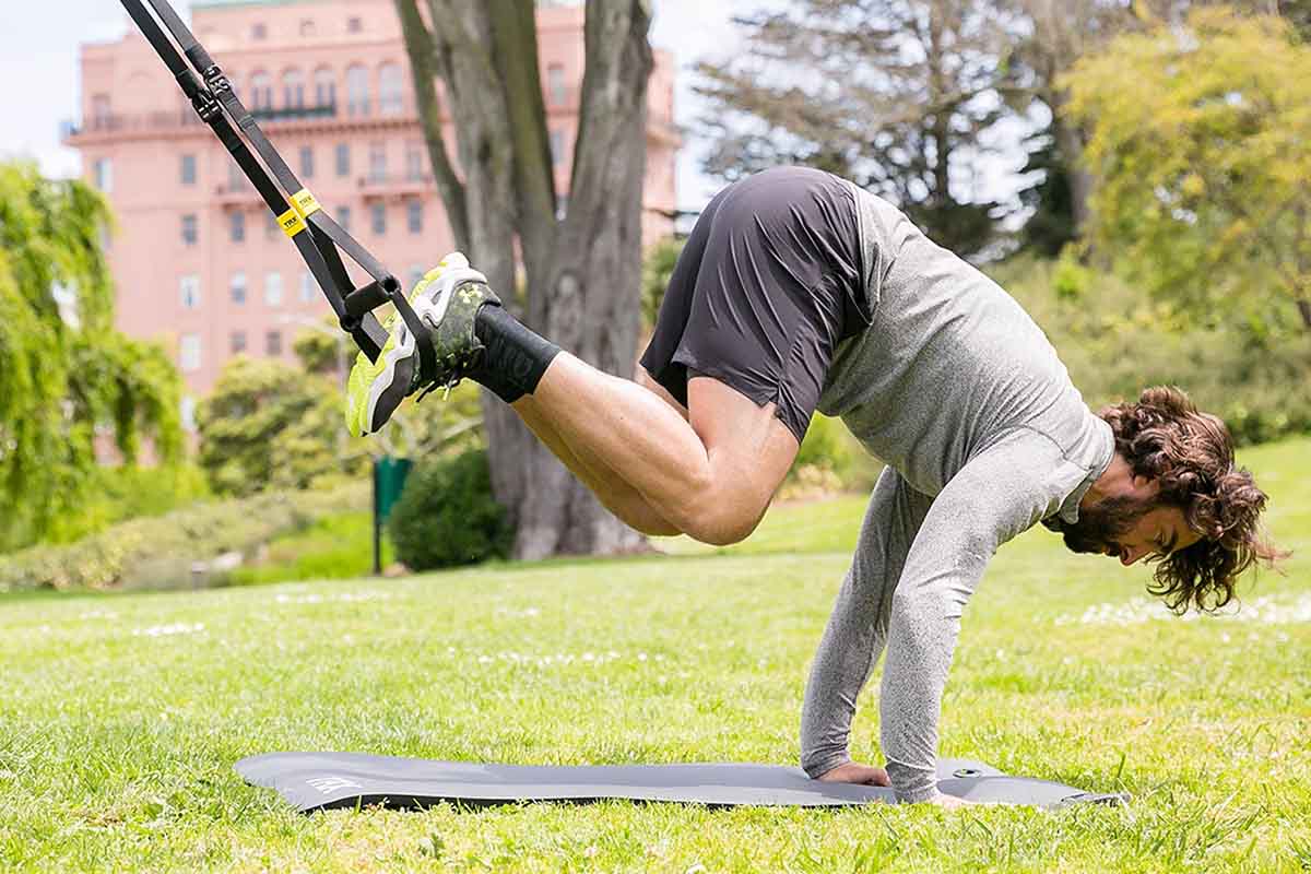 A man using the TRX GO Suspension Trainer System — now on sale at Woot — outside in a park.
