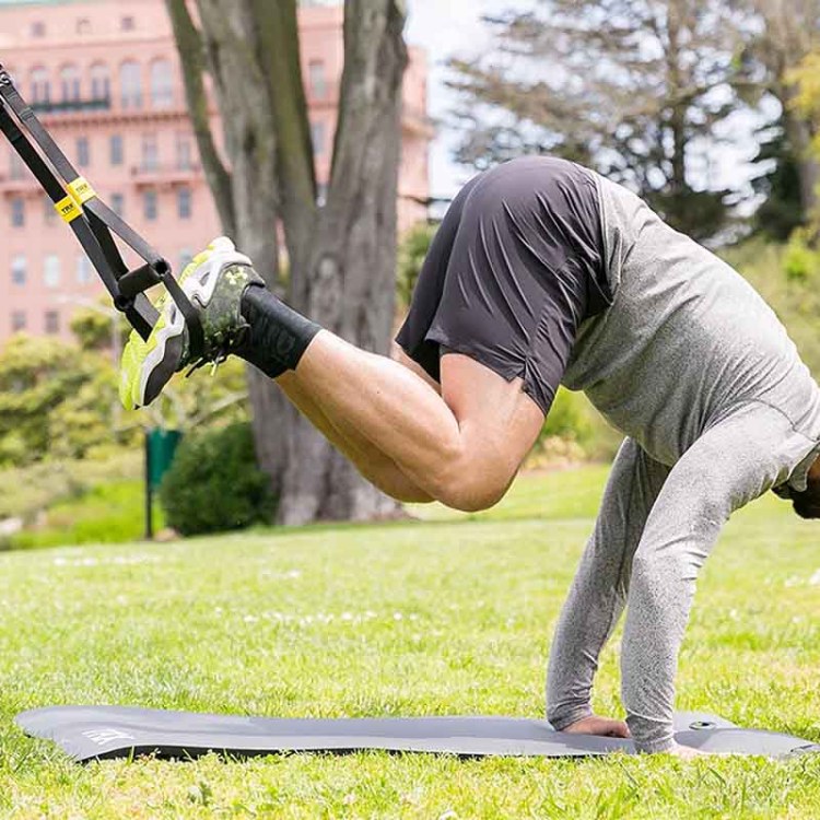 A man using the TRX GO Suspension Trainer System — now on sale at Woot — outside in a park.