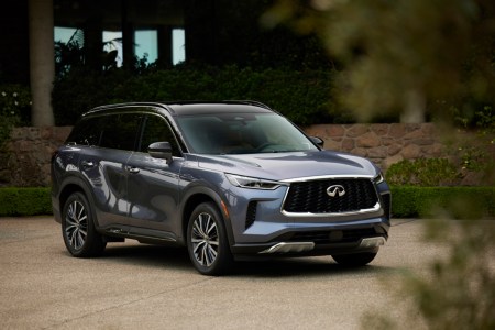 The all-new 2022 Infiniti QX60 luxury crossover sitting in a driveway next to a house with some greenery in the foreground