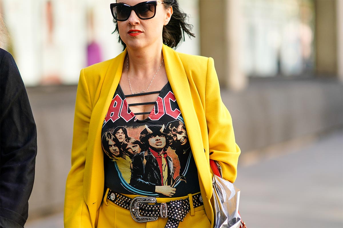 A guest wears sunglasses, an AC DC t-shirt, a studded belt, a yellow oversized blazer jacket, yellow pants, during London Fashion Week September 2019