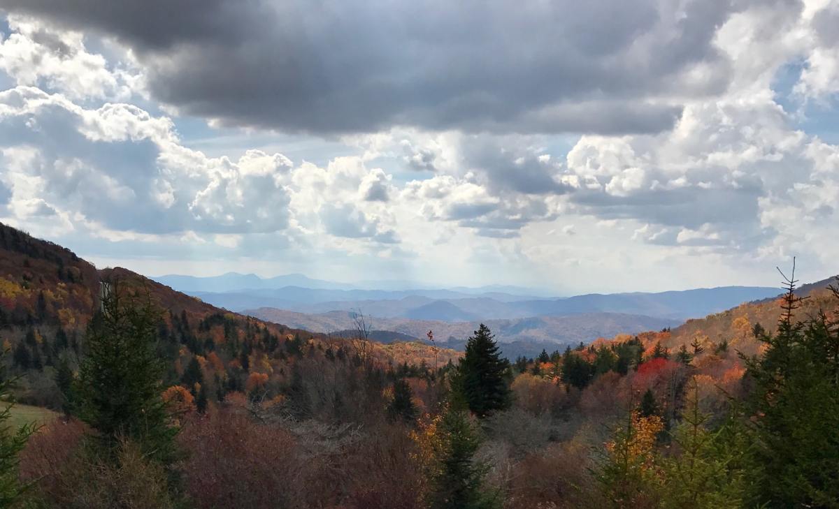 A view of a valley along the Appalachian Trail with white clouds in a blue sky and lots of trees with leaves changing colors