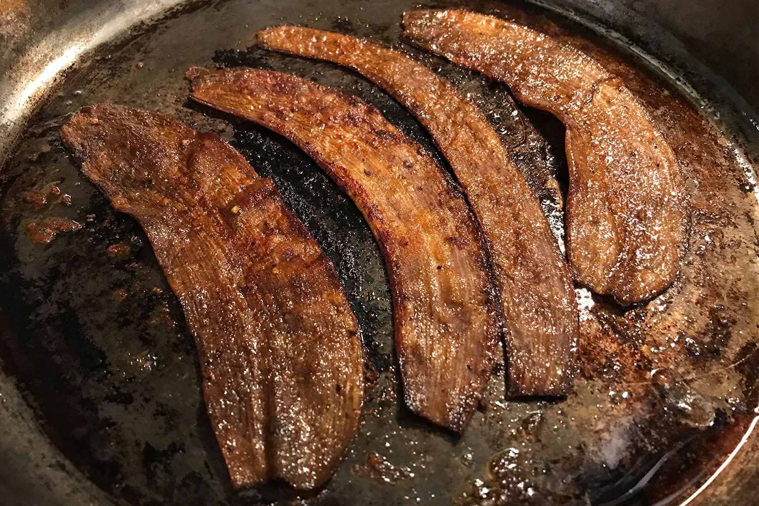 A Smithey cast iron skillet with four piece of banana peel bacon. Yes, the fruit, fake meat, vegetarian and vegan bacon tasted good, if you follow this recipe.