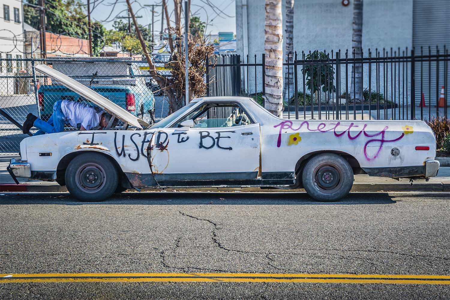 A used car with spray paint on it that reads "I used to be pretty"
