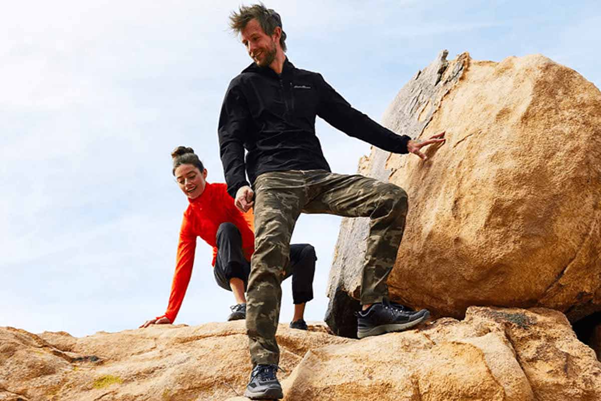 A woman and a man climbing rocks in Eddie Bauer gear. Eddie Bauer clothing is on sale as part of an end-of-season sale.