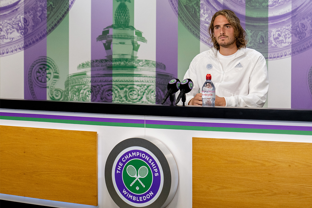 Pro tennis player Stefanos Tsitsipas sitting behind a table at Wimbledon and answering questions about why he won't take the COVID-19 vaccine