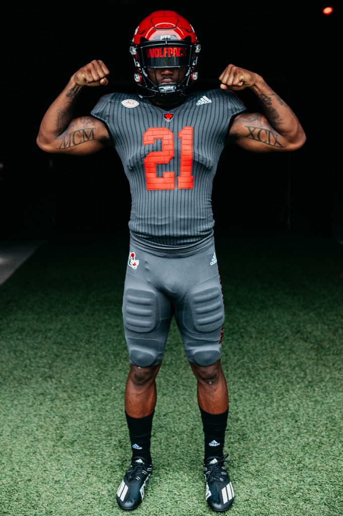 an nc state football player flexes while wearing the team's new uniforms for 2021