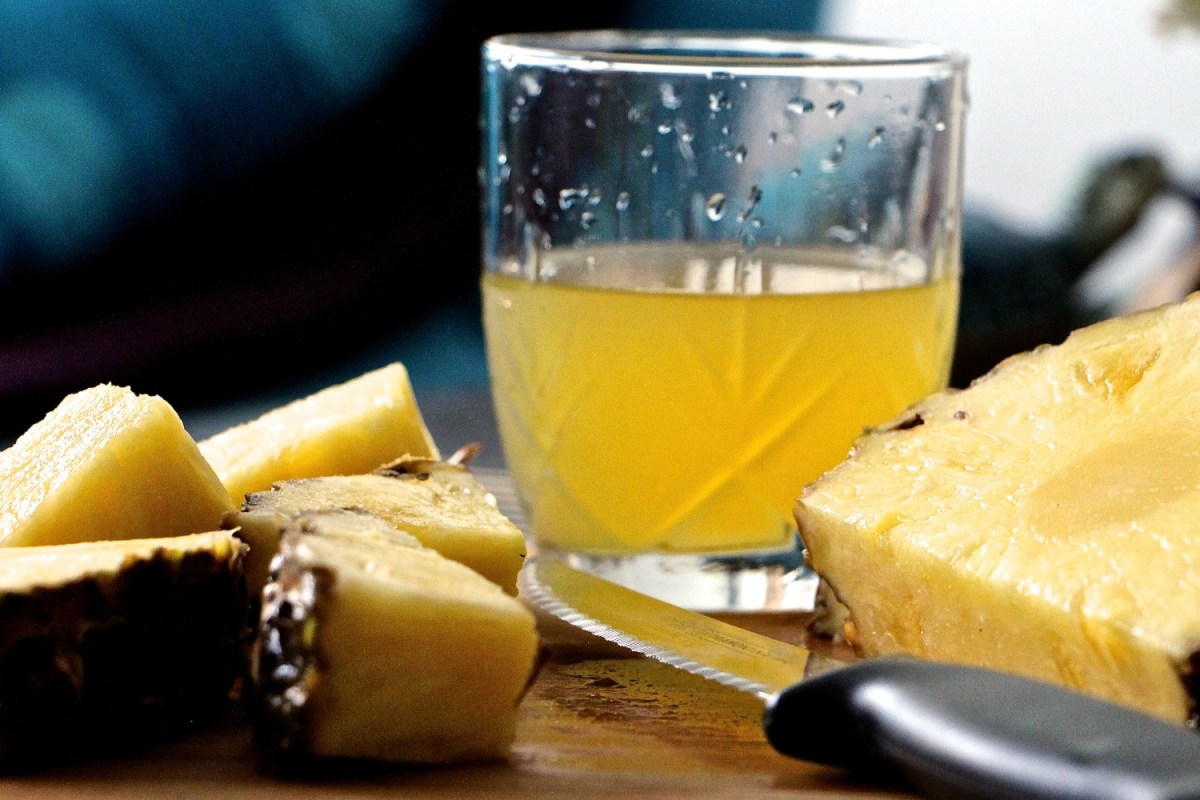 Glass of pineapple juice on table with sliced pineapple