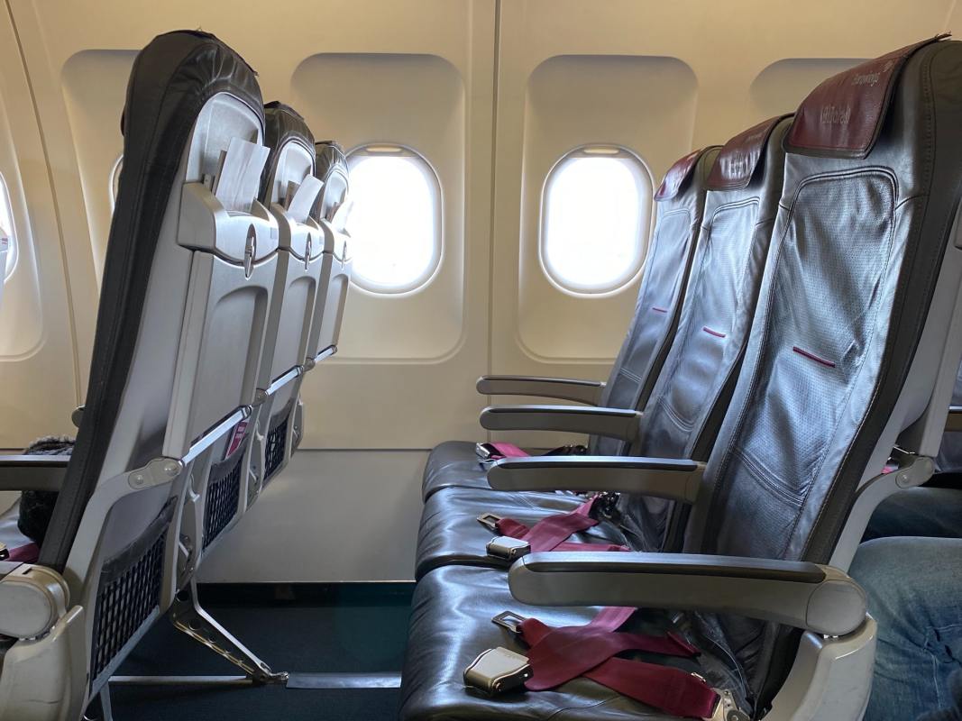 A row of three empty airplane seats without passengers in a commercial airliner with light coming in through the open windows