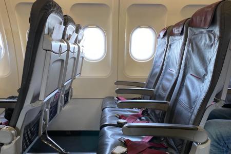 A row of three empty airplane seats without passengers in a commercial airliner with light coming in through the open windows