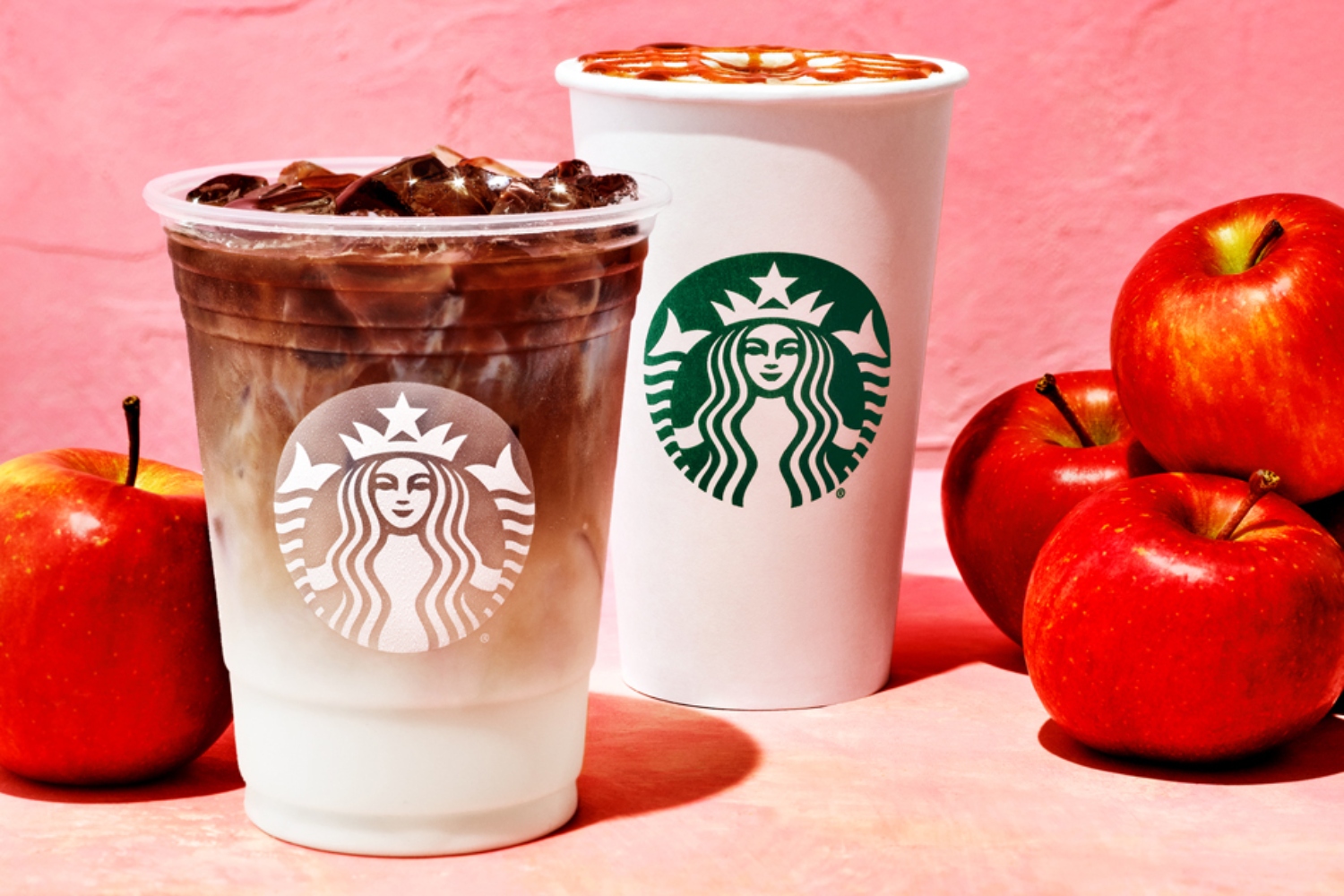 hot and iced versions of starbuck's new apple crisp macchiato on display, surrounded by apples