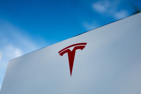 The red Tesla "T" logo on a white building in California. Elon Musk's EV company is under investigation for crashes involving Autopilot and other driver assist features, announced in August 2021.