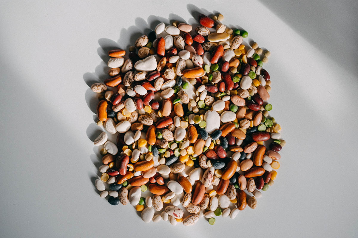 A pile of dry beans of all colors ranging from brown to green against a white background