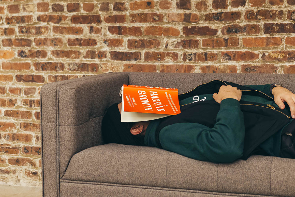 A man lies on the couch with a book over his face