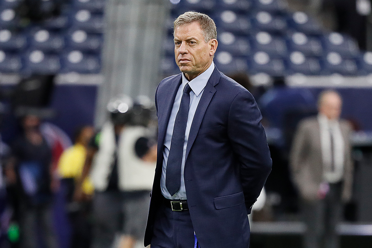Former NFL quarterback Trok Aikman standing on a football field in a suit before a game