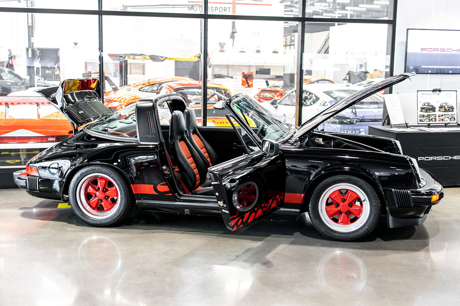 A 1989 Porsche 911 Targa G-Model in red and black restored by Porsche Ontario for the Porsche Classic Restoration Challenge sitting in front of a bunch of other sports cars