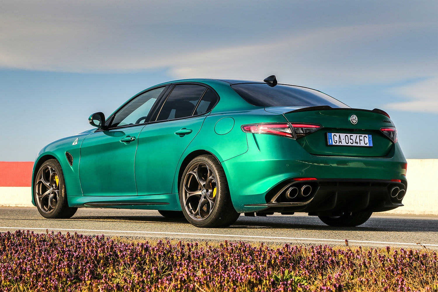 The 2021 Alfa Romeo Giulia Quadrifoglio sport sedan in green shot from the back left sitting on a racetrack surrounded by grass