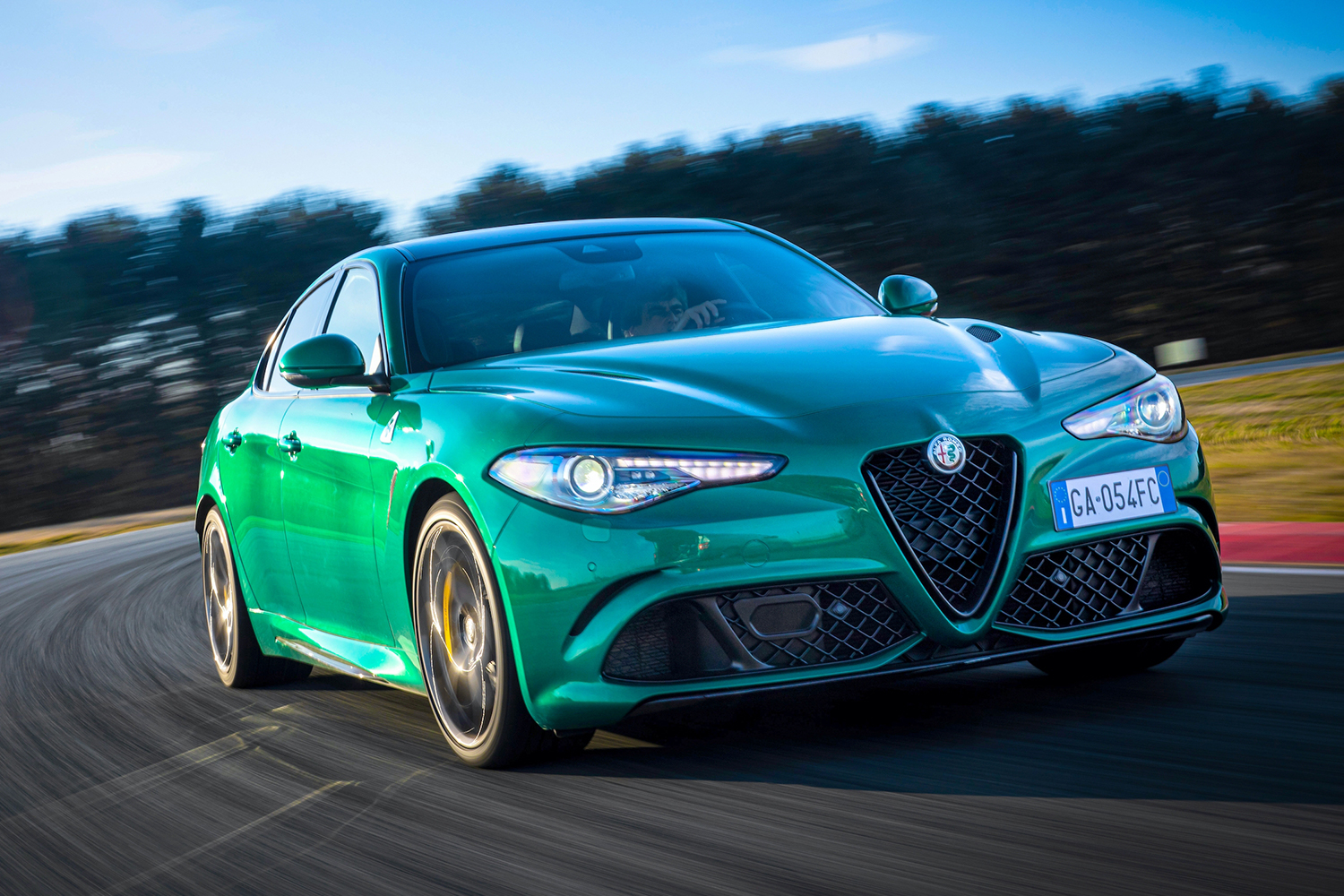 A green 2021 Alfa Romeo Giulia Quadrifoglio turning left around a race track with trees blurred in the background
