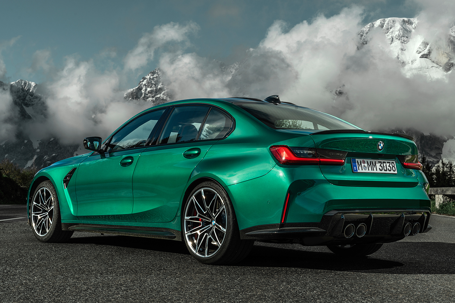 The new BMW M3 Competiton Sedan in green sits on the road with snow-capped mountains covered in clouds in the background