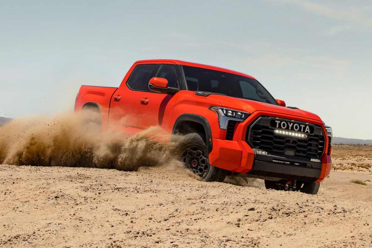 The new 2022 Toyota Tundra pickup in the color Solar Octane driving through the sand and kicking up dirt