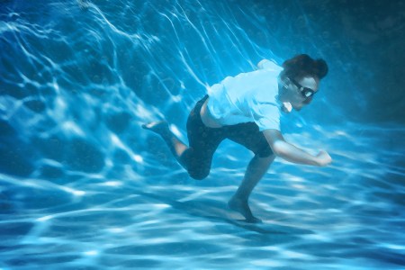 A man in goggles runs on the surface of a pool.
