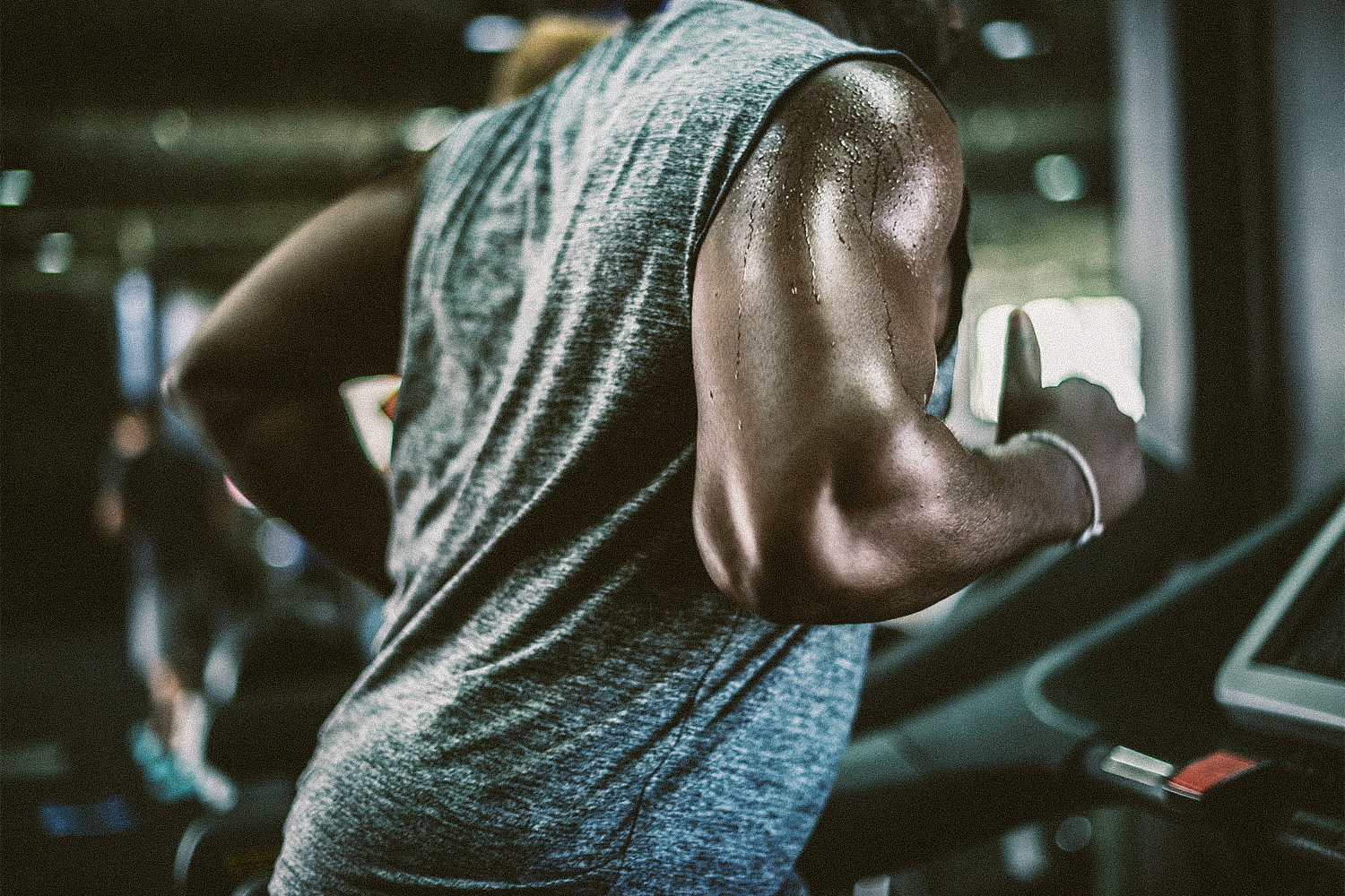 A sweaty man in a sleeveless shirt runs on a treadmill.