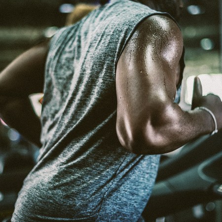 A sweaty man in a sleeveless shirt runs on a treadmill.