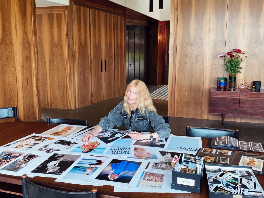 Supermodel Claudia Schiffer sitting at a table featuring dozens of fashion photographs from the 1990s, some of which will go into her exhibit "Captivate!" and accompanying coffee table book