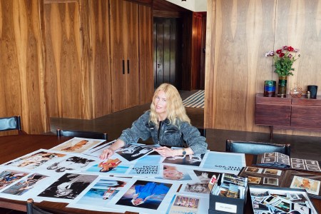 Supermodel Claudia Schiffer sitting at a table featuring dozens of fashion photographs from the 1990s, some of which will go into her exhibit "Captivate!" and accompanying coffee table book