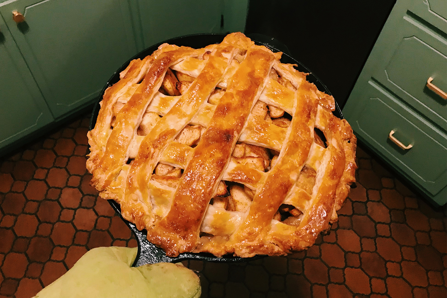 A Field Company No. 8 cast iron skillet holding an apple pie fresh out of the oven, with green cabinets and a geometric floor in the background