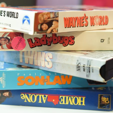 A stack of retro VHS tapes including Wayne's World, Ladybugs, Twins, Son in Law and Home Alone