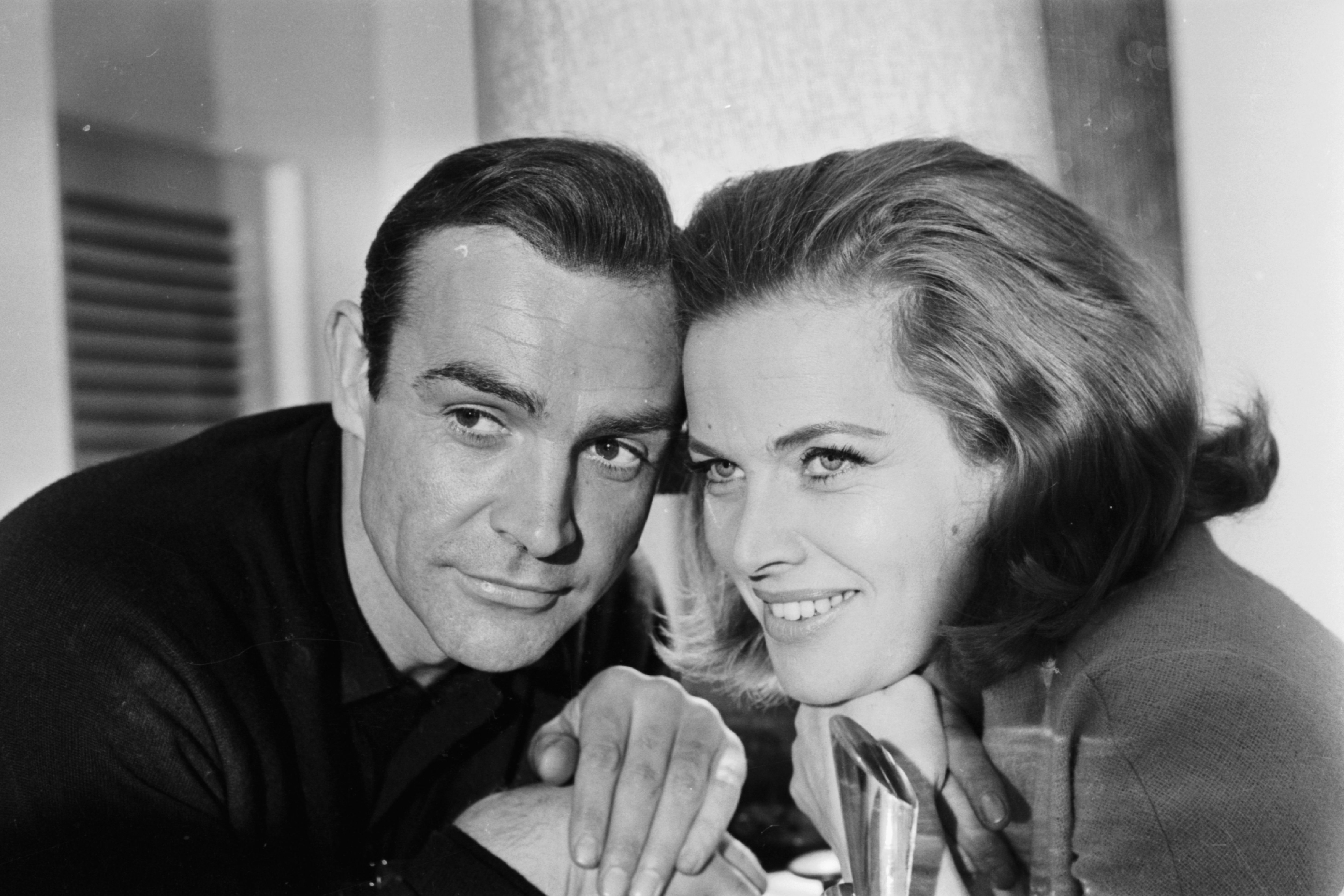 A black and white photo of Sean Connery (James Bond) and Honor Blackman (Pussy Galore) promoting the film "Goldfinger" in 1964