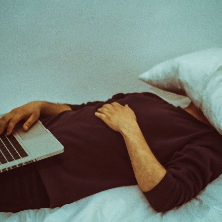 A man sleeps with a pillow on his face and a computer on his lap.