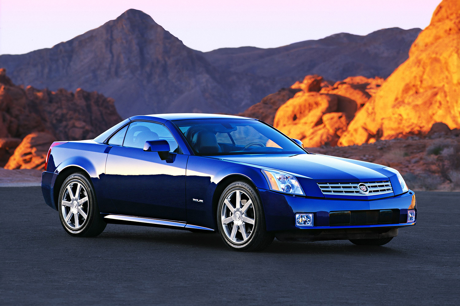 The ill-fated 2004 Cadillac XLR sitting still on the concrete at sunset with desert hills in the background