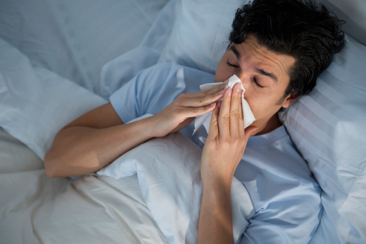 Man in bed blowing nose into tissue