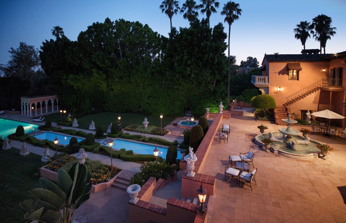The terrace of the Hearst Estate at sunset featuring a fountain, multiple pools and lush greenery with palm trees in the background against a blue sky