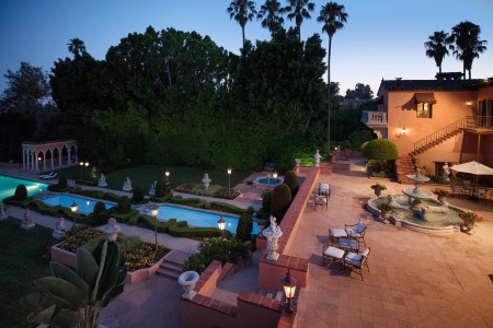 The terrace of the Hearst Estate at sunset featuring a fountain, multiple pools and lush greenery with palm trees in the background against a blue sky